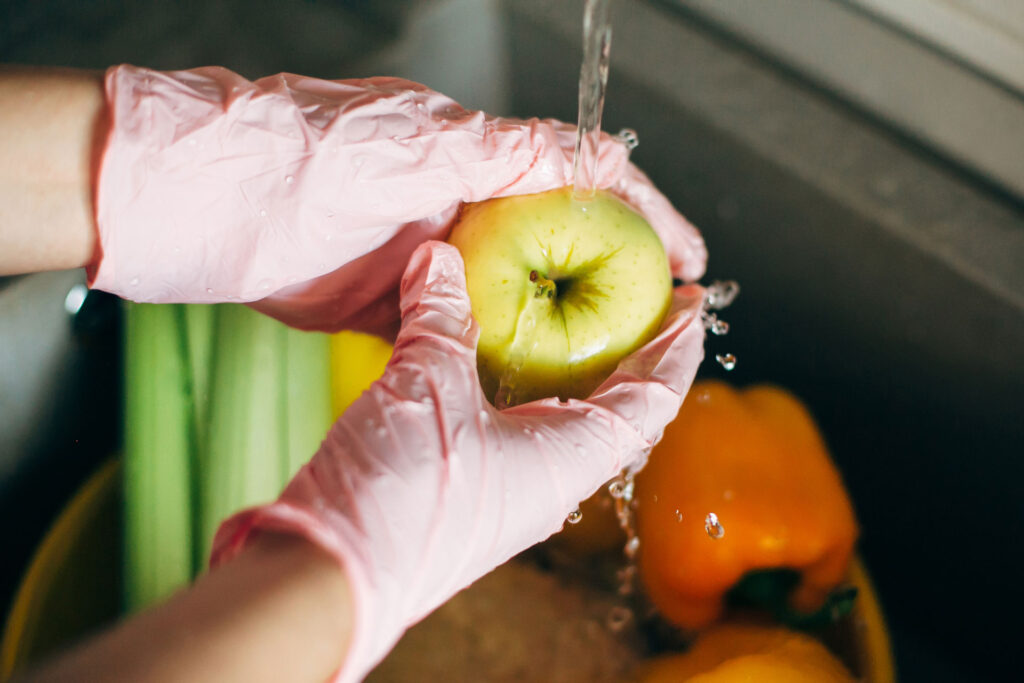 washing fruit under a sink wearing pink gloves