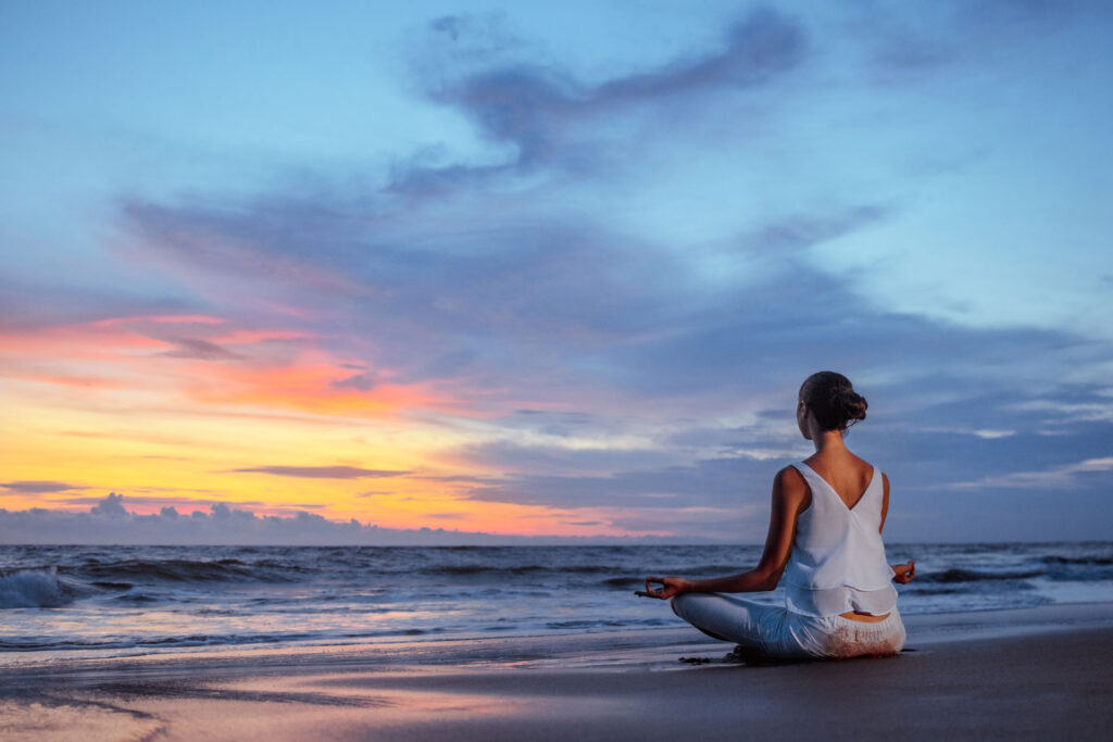 female meditating on beach during a sunset