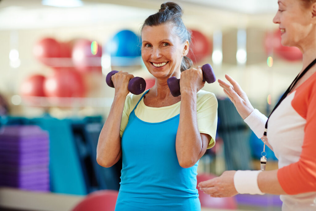 senior female lifting weights with personal trainer