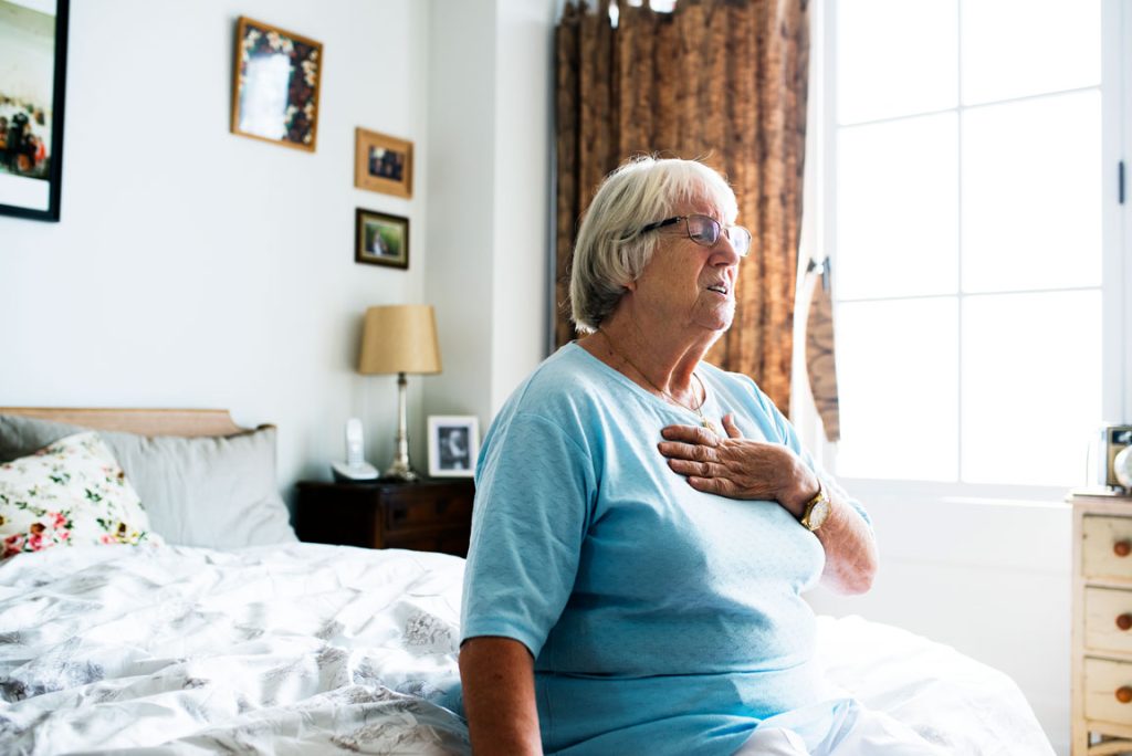 senior woman experiencing heart problems while sitting in bed