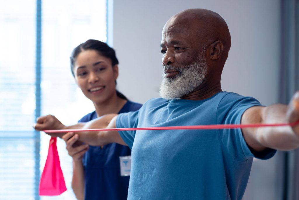 smiling-diverse-female-physiotherapist-helping-senior older adult African American stretching with trainer