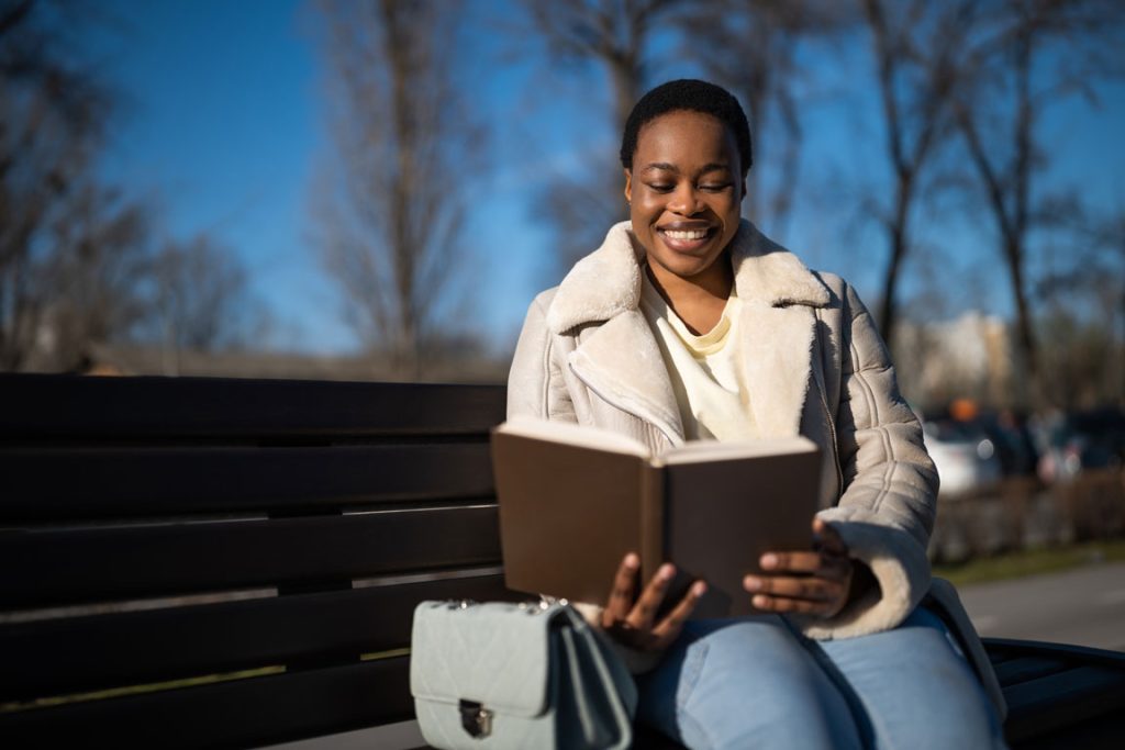 relaxation-outdoor African American woman reading book outdoors on bench