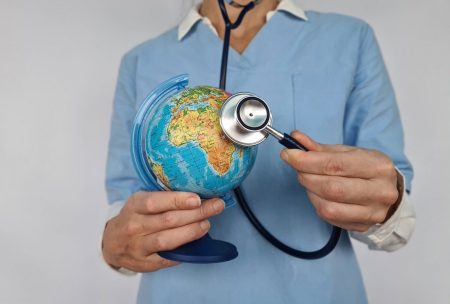 doctor holding stethoscope to globe